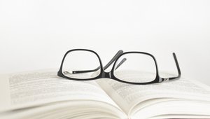 Prüfkriterien: Brille, auf einem aufgeschlagenen Buch liegend.